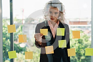 Caucasian businesspeople with glass board and post it note having brainstorming in workplace