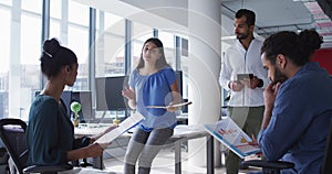 Caucasian businesswoman holding file and talking to diverse colleagues at casual office meeting