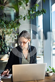 Caucasian businesswoman working at her desk in cafe. Female executive looking away and smiling. Woman working on laptop sitting at