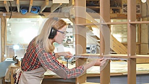 Caucasian carpenter woman measuring handmade wooden shelf with tape-line.
