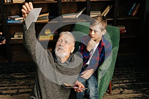 Caucasian cheerful gray-haired grandfather with grandson enjoy memories watching family photo album