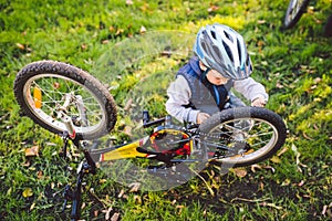 Caucasian child boy in a helmet learns to repair his bike. Child cyclist checks the mechanism of a bicycle in a clearing of green