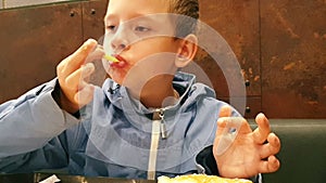 Caucasian child in a cafe eats French fries with appetite, dips in sauce. The boy has breakfast in a fast food cafe. Delicious cri