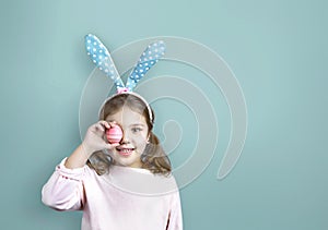 Caucasian child girl holding Easter egg on blue empty space background. Happy cute smiling bunny kid easter backdrop