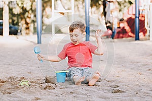 Caucasian child sitting in sandbox playing with beach toys. Baby building sandcastle sand pie. Little boy have fun on playground.