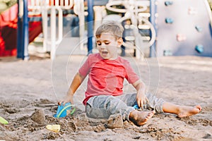 Caucasian child sitting in sandbox playing with beach toys. Baby building sandcastle sand pie. Little boy have fun on playground.