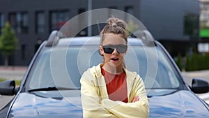 Caucasian cool young teen girl standing in front of car on street looking at camera chewing a gum. Close up. Stylish