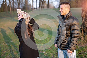 Caucasian couple in casual wear is in the spring park. Happy and smiling they joke among themselves: he pretends to puddle her and