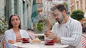 Caucasian couple eat breakfast in city cafe outdoors addicted busy man boyfriend using mobile phone ignoring upset woman