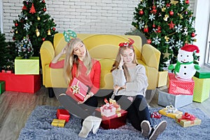 Caucasian couple girls friends sitting on the floor and holding big Gift boxes in Christmas party. They are drunk and bored.