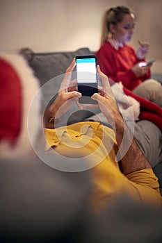 Caucasian couple at home for christmas, typing on their cell phones. Corona, covid conpect