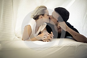 Caucasian couple kissing under the sheets on the bed at home in the bedroom - intimate lifestyle for young people in love -