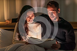 Caucasian couple lying on bed reading book in bedroom together