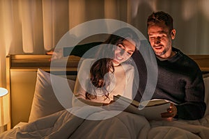 Caucasian couple lying on bed reading book in bedroom together