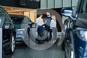 A caucasian couple shakes hands with a salesperson while buying a car.