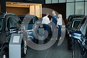 A caucasian couple shakes hands with a salesperson while buying a car.