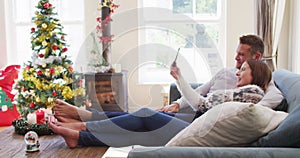 Caucasian couple smiling and waving while having a video call on smartphone sitting on the couch at