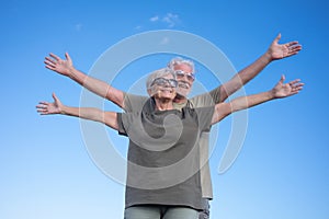 Caucasian couple of two happy senior people enjoying outdoors and nature, standing with open arms feeling freedom. Smiling white-