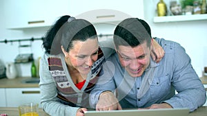 Caucasian couple is using computer at kitchen. Home, technology and relationships concept - smiling husband and wife