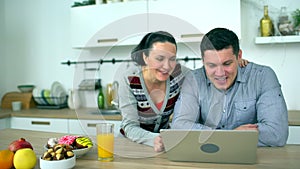 Caucasian couple is using computer at kitchen. Home, technology and relationships concept - smiling husband and wife