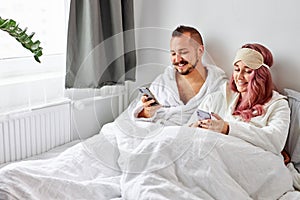Caucasian couple using smartphone lying on bed together, checking social networks news