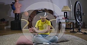 Caucasian curly-haired boy touching something invisible as using VR headset. Cute schoolboy in casual clothes moving his