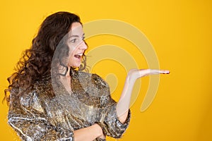 Caucasian curly smiling woman pretending to hold something on the palm isolated on yellow studio background
