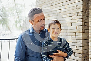 Caucasian dad hugging his cute smiling son. Young man communicates with a little boy on the porch of the house