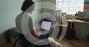 Caucasian disabled man sitting in wheelchair using laptop in bedroom