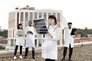 Caucasian doctor holding x-ray scan of patient during break outdoors hospital.