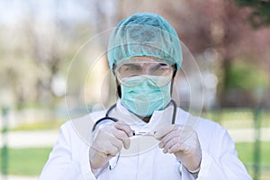 Caucasian Doctor male with a mask and scrub cap holding a Coronavirus Covid-19