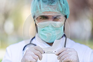 Caucasian Doctor male with a mask and scrub cap holding a Coronavirus Covid-19 with blur background