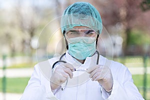 Caucasian Doctor male with a mask and scrub cap holding a Coronavirus Covid-19 with blur garden