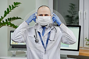 A caucasian doctor putting on a protective face mask to examine a patient