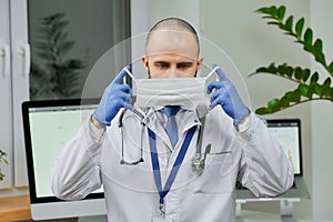 A caucasian doctor putting on a protective face mask to examine a patient