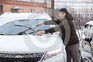 Caucasian driver cleans windshield and removes snow from rubber wipers of his car