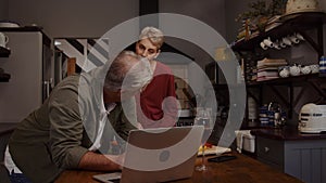 Caucasian elderly couple cooking in kitchen using laptop