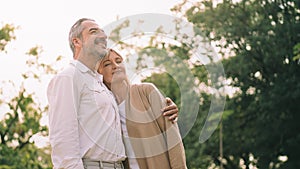 Caucasian elderly couple is standing, holds each other and smiling upward enjoy spending time together with happiness, a happily