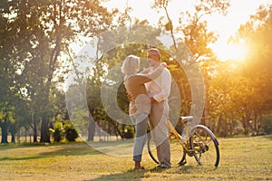 The Caucasian elderly couples standing beside a bicycle in the natural autumn sunlight garden and looking each other feel cherish