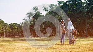 The Caucasian elderly couples standing beside a bicycle in the natural autumn sunlight garden and turn them face toward to camera