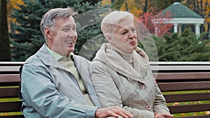 Caucasian elderly family rest time together in autumn park sit on bench married couple partners senior aged man hugs