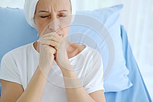 Caucasian Elderly Mother in white headscarf is laying on bed in hospital after chemotherapy because she is holding her hand for