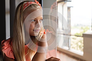 Caucasian elementary schoolgirl leaning on glass window in classroom