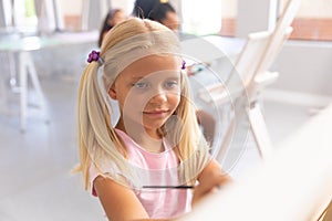 Caucasian elementary schoolgirl painting on easel during drawing class in school