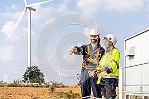 Caucasian engineer man discuss together with co-worker woman hold tablet and blueprint stay in front of row of windmill