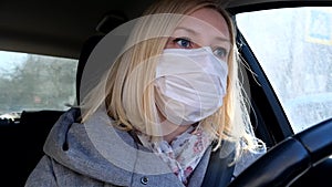 Caucasian european woman driving a car and wearing white surgical medical face mask as a way of protection against coronavirus and