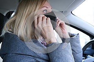 Caucasian european woman sitting in a car and putting on black surgical medical face mask as a way of protection against
