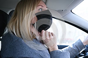 Caucasian european woman sitting in a car and putting on black surgical medical face mask as a way of protection against