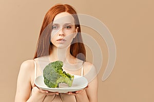 Anorexic woman in underwear holding plate with raw broccoli isolated in studio photo
