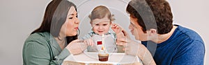 Caucasian family with baby boy celebrating his first birthday at home. Mother father dad with child kid toddler blowing candle on